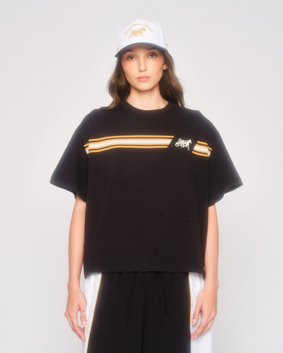 Model wearing the black Speed Racer cropped tee with a white cap and black and white track pants