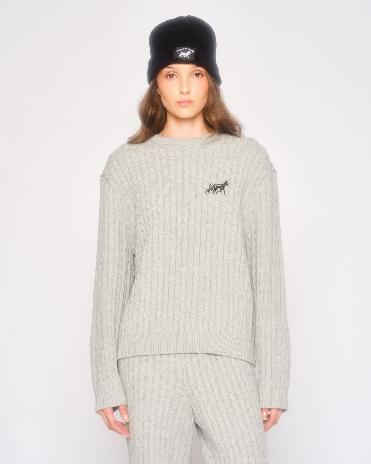 Model wearing the grey cable knit sweater with matching grey cable knit pants and a black beanie