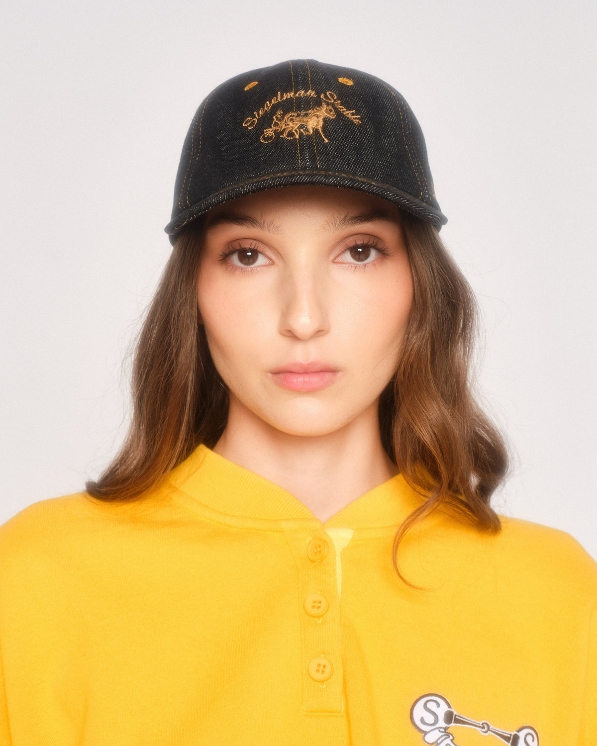 Model wearing the black contrast denim dad hat with gold embroidery and a yellow henley sweatshirt