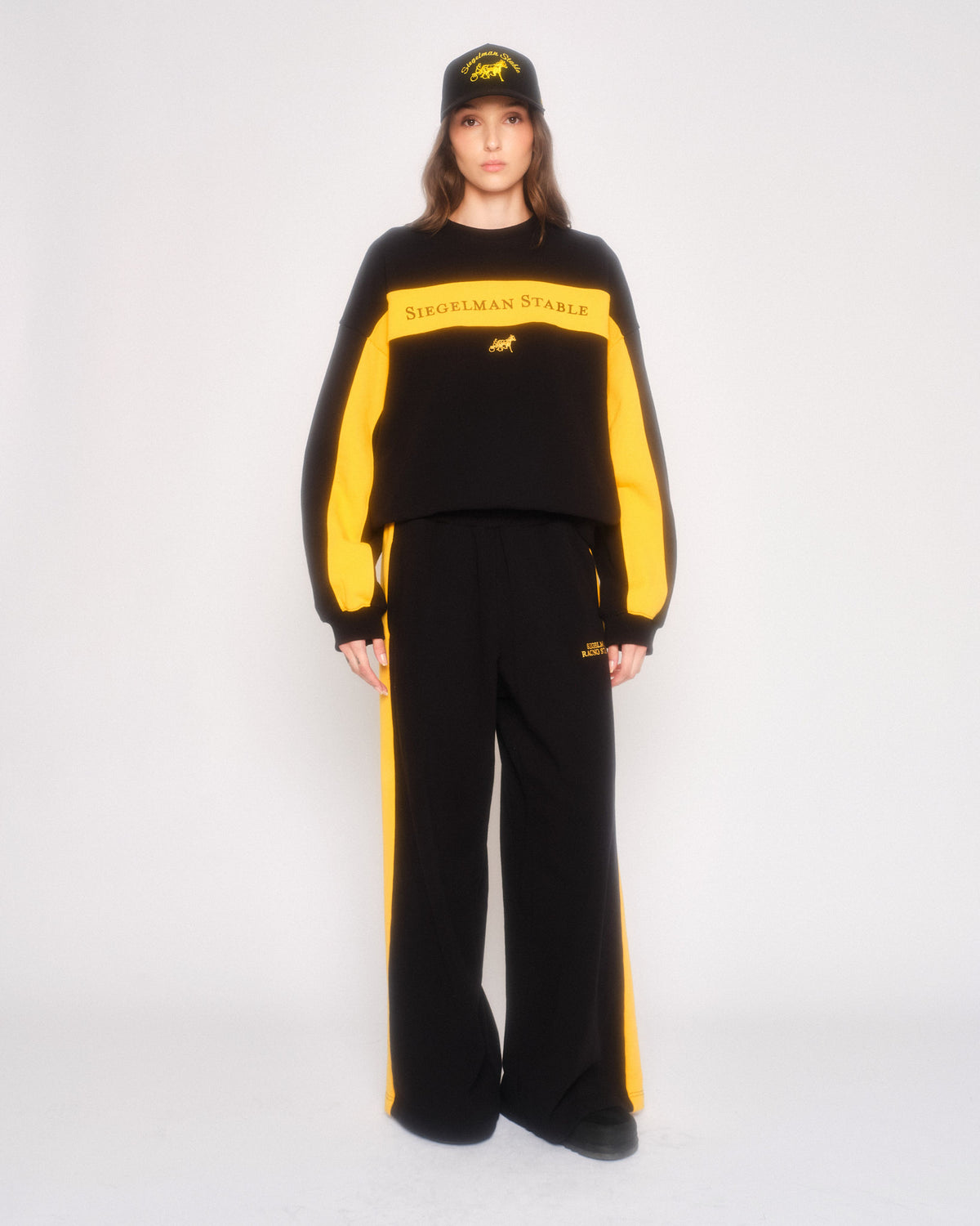 Model wearing the black retro sweatpants with yellow side stripes, matching crewneck and black cap