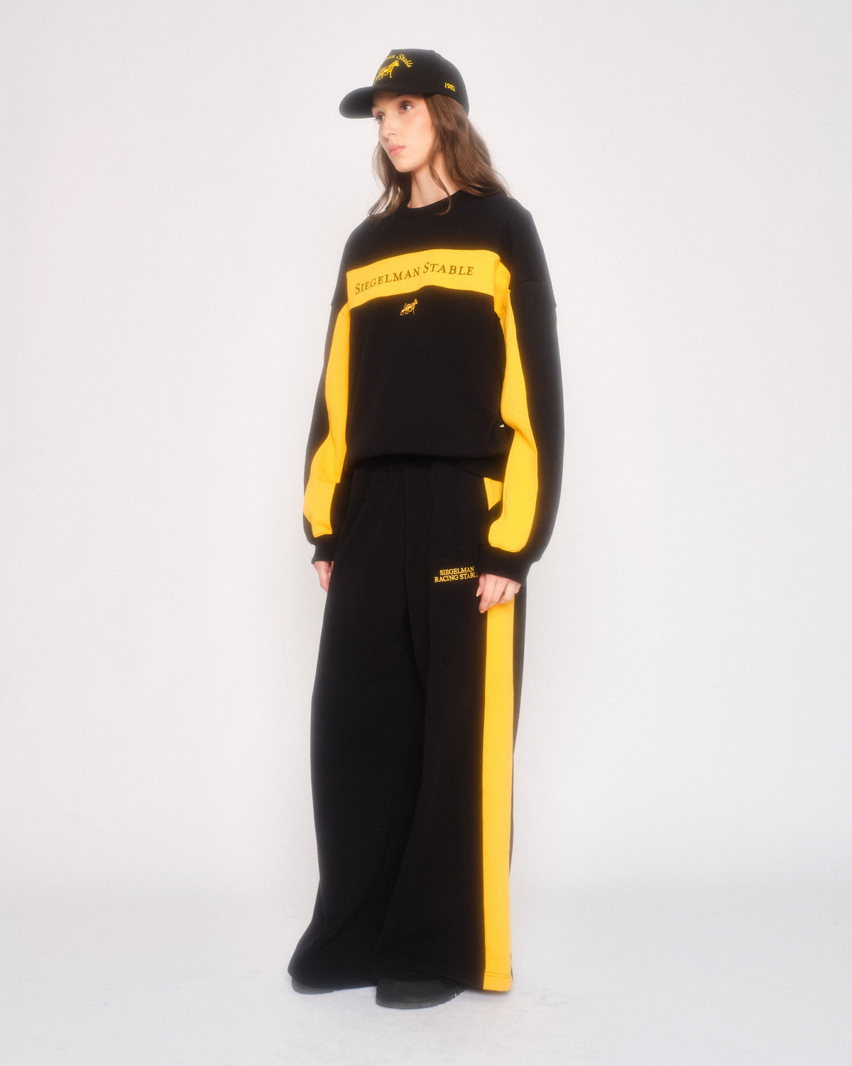 Model in profile wearing the black and yellow retro sweatpant set and a black cap