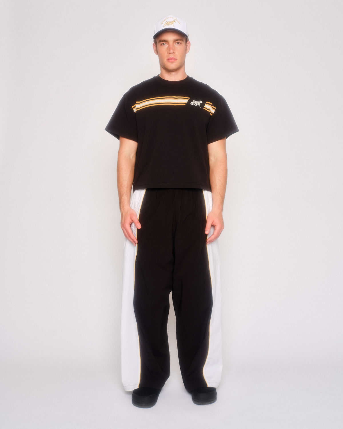 Male model wearing the black track pants with white side panels and a black tee with striped chest graphic