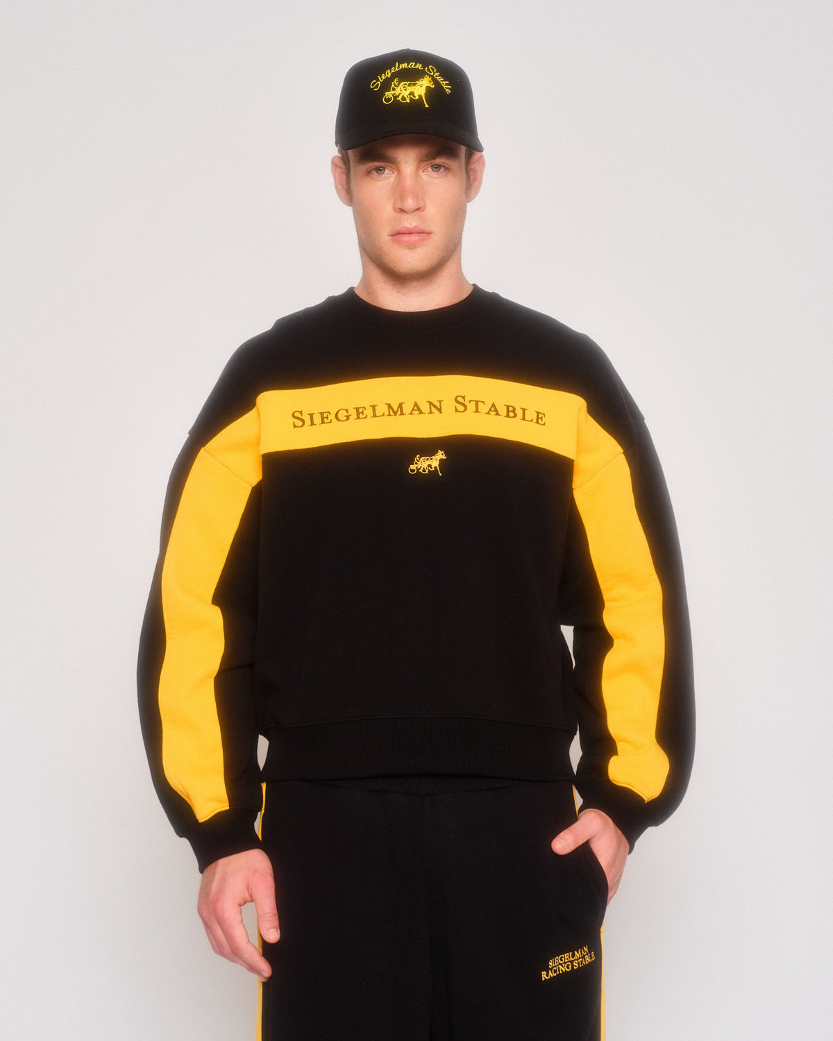 Male model wearing the black and yellow retro crewneck with matching sweatpants and a black cap