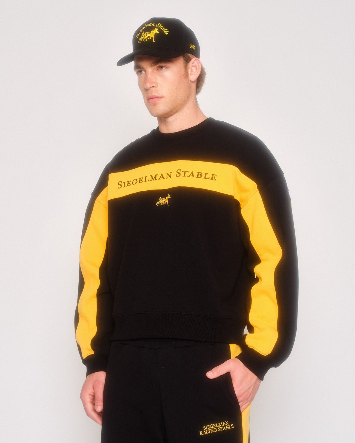 Male model in three-quarter view wearing the black retro crewneck with yellow stripes and black cap