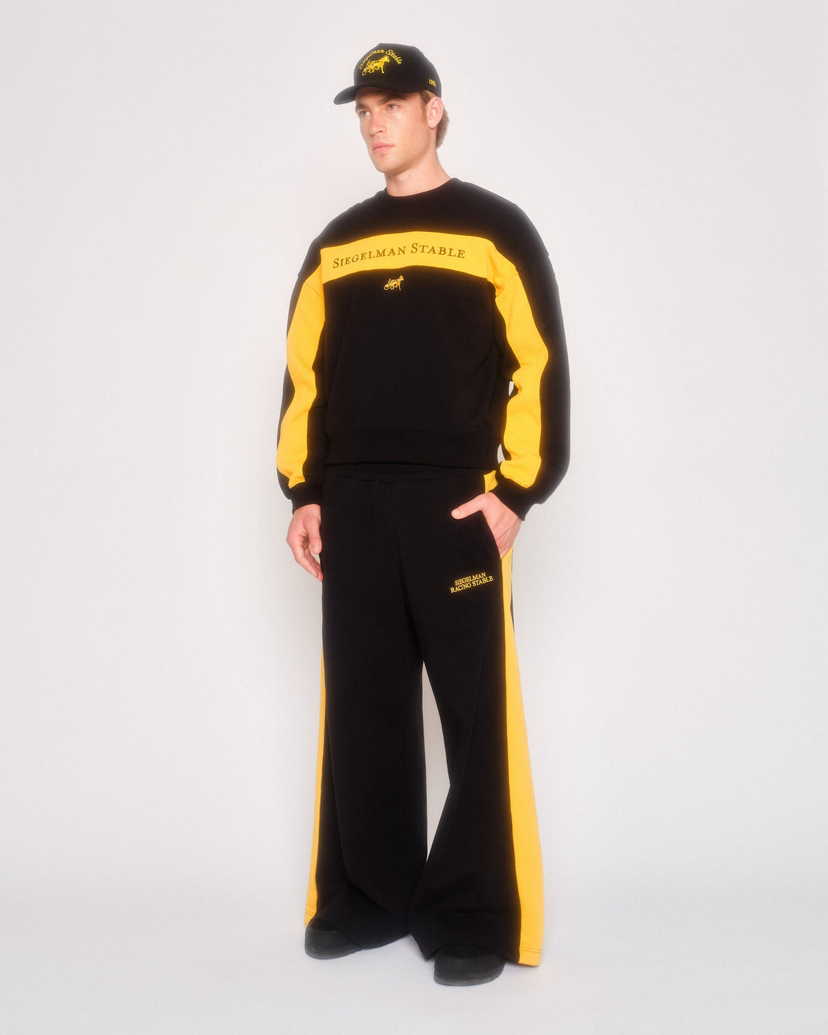 Male model in three-quarter view wearing the black and yellow retro sweatpants, crewneck and black cap