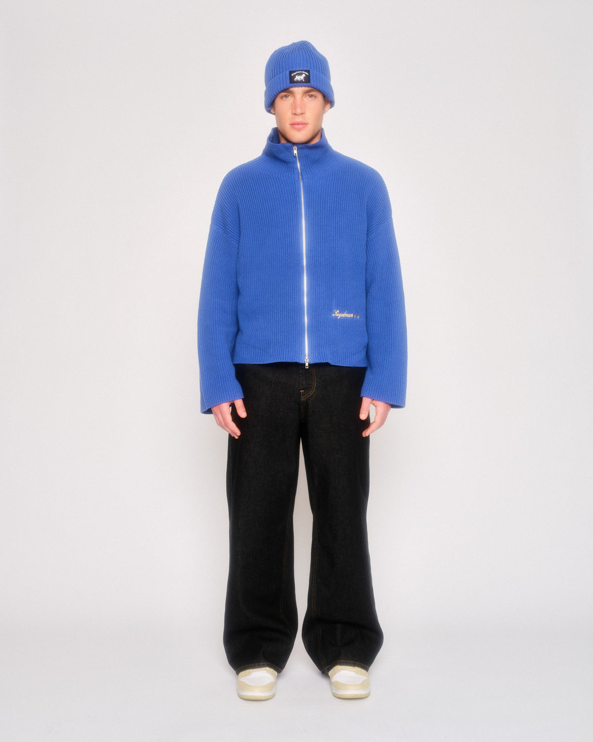 Model wearing the black straight leg jeans with a cobalt blue zip fleece jacket, blue beanie and white sneakers