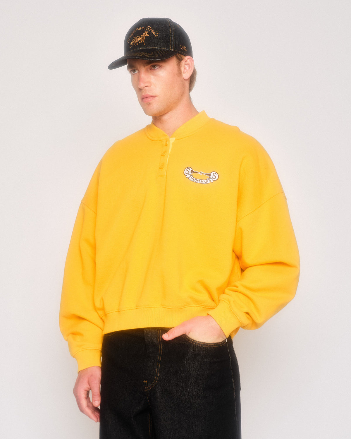 Male model in three-quarter view wearing the yellow Siegelman Stable henley and a black cap