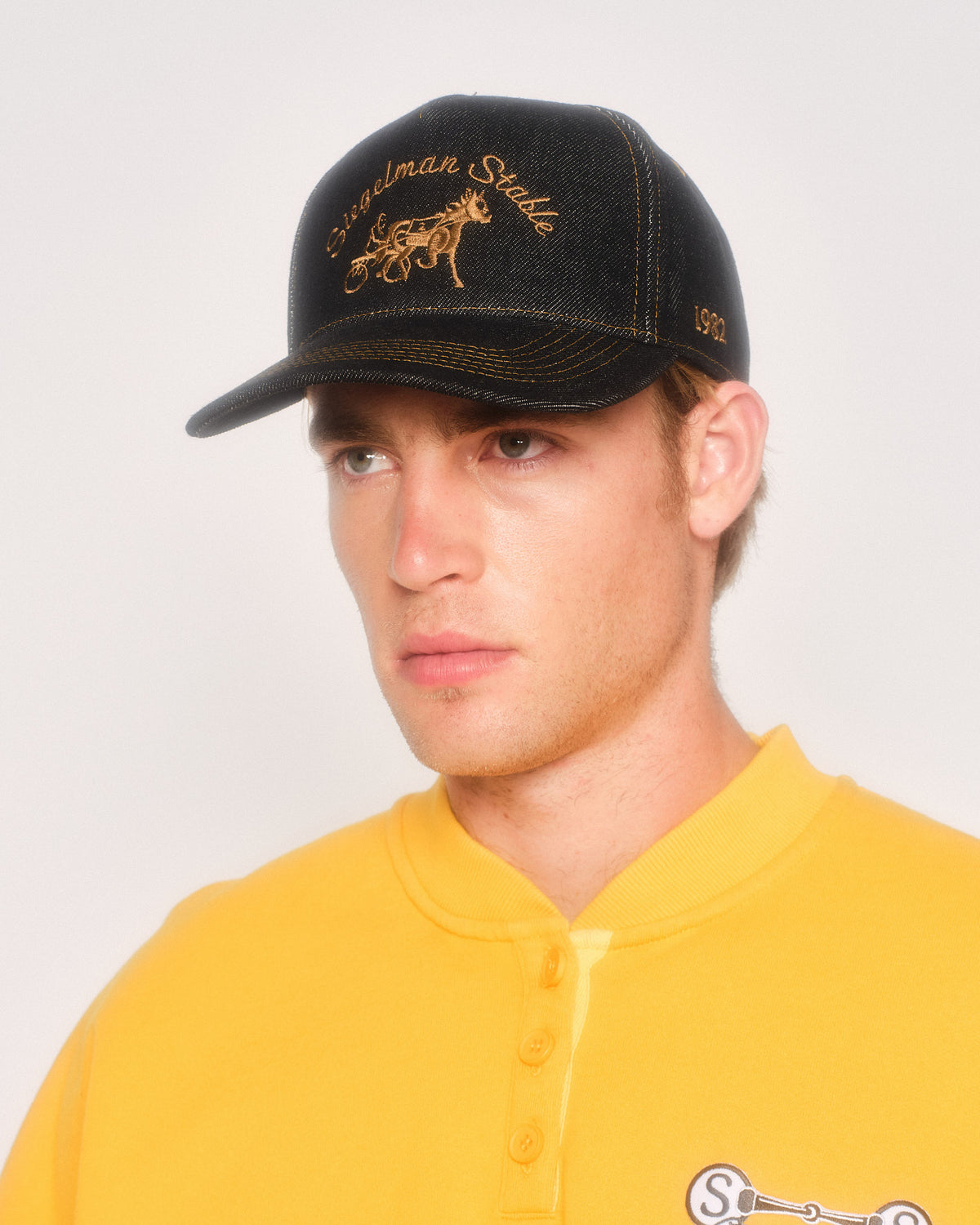 Male model in three-quarter view wearing the black denim hat with gold contrast stitching