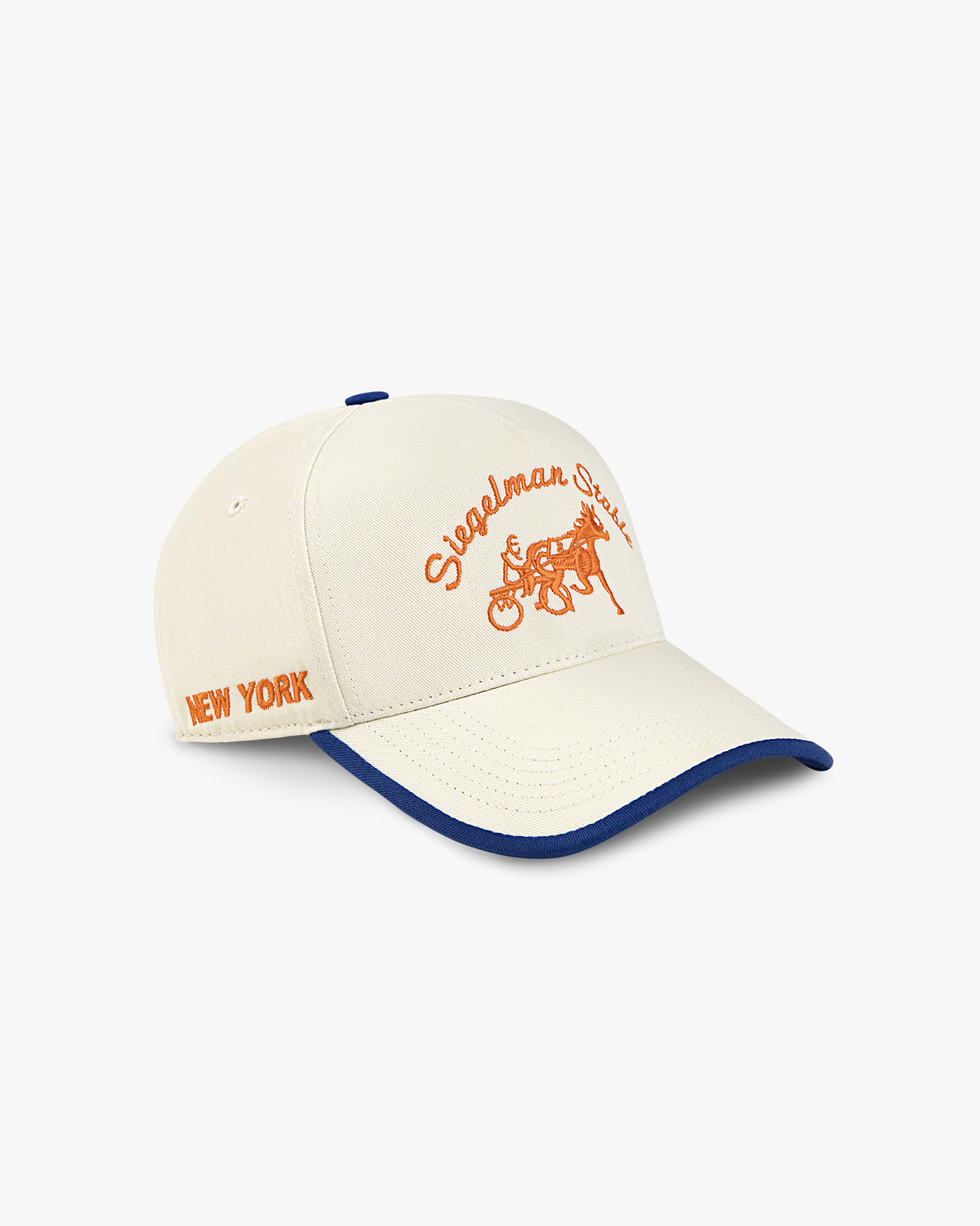 Three-quarter view of the cream and royal 2026 Champions hat with orange NEW YORK side embroidery