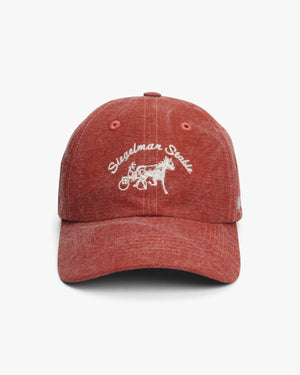 Front view of a red washed canvas dad hat with cream Siegelman Stable script and horse and sulky embroidery