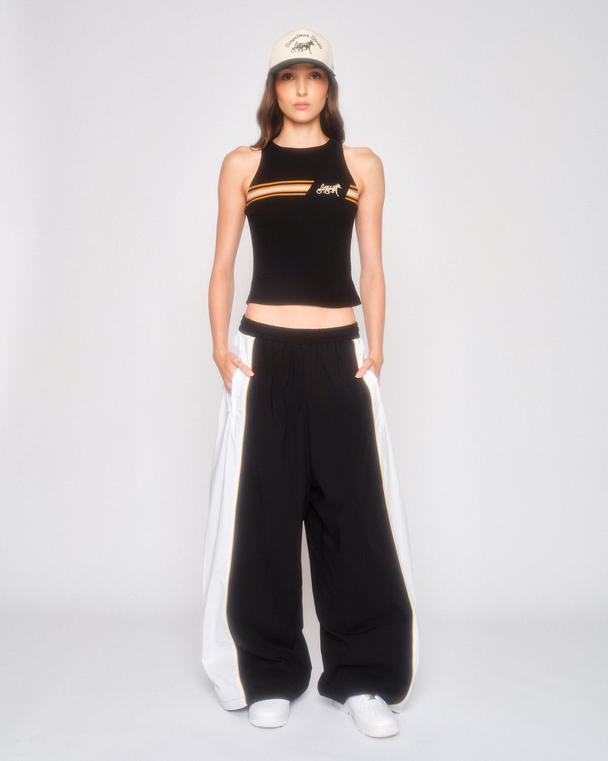 Model wearing the black and white wide leg track pants with a black cropped tank and white cap