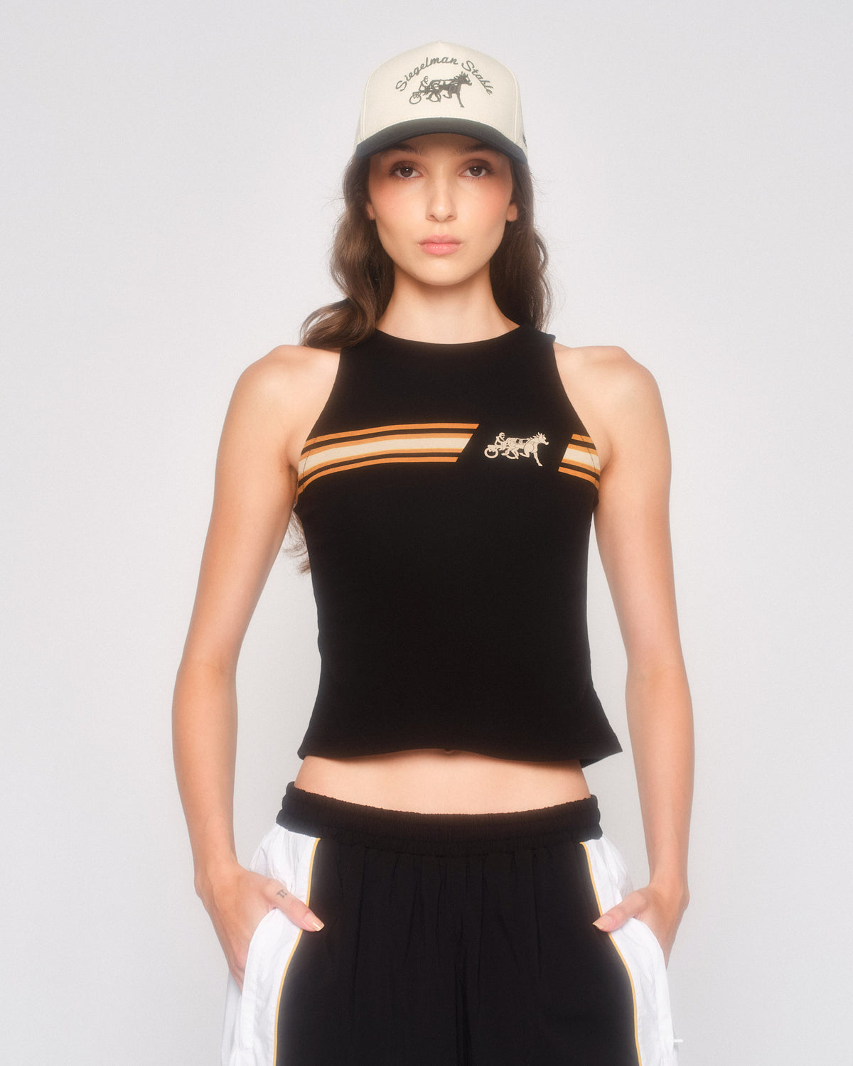 Model wearing the black Speed Racer tank with striped chest graphic, a cream cap and black and white track pants