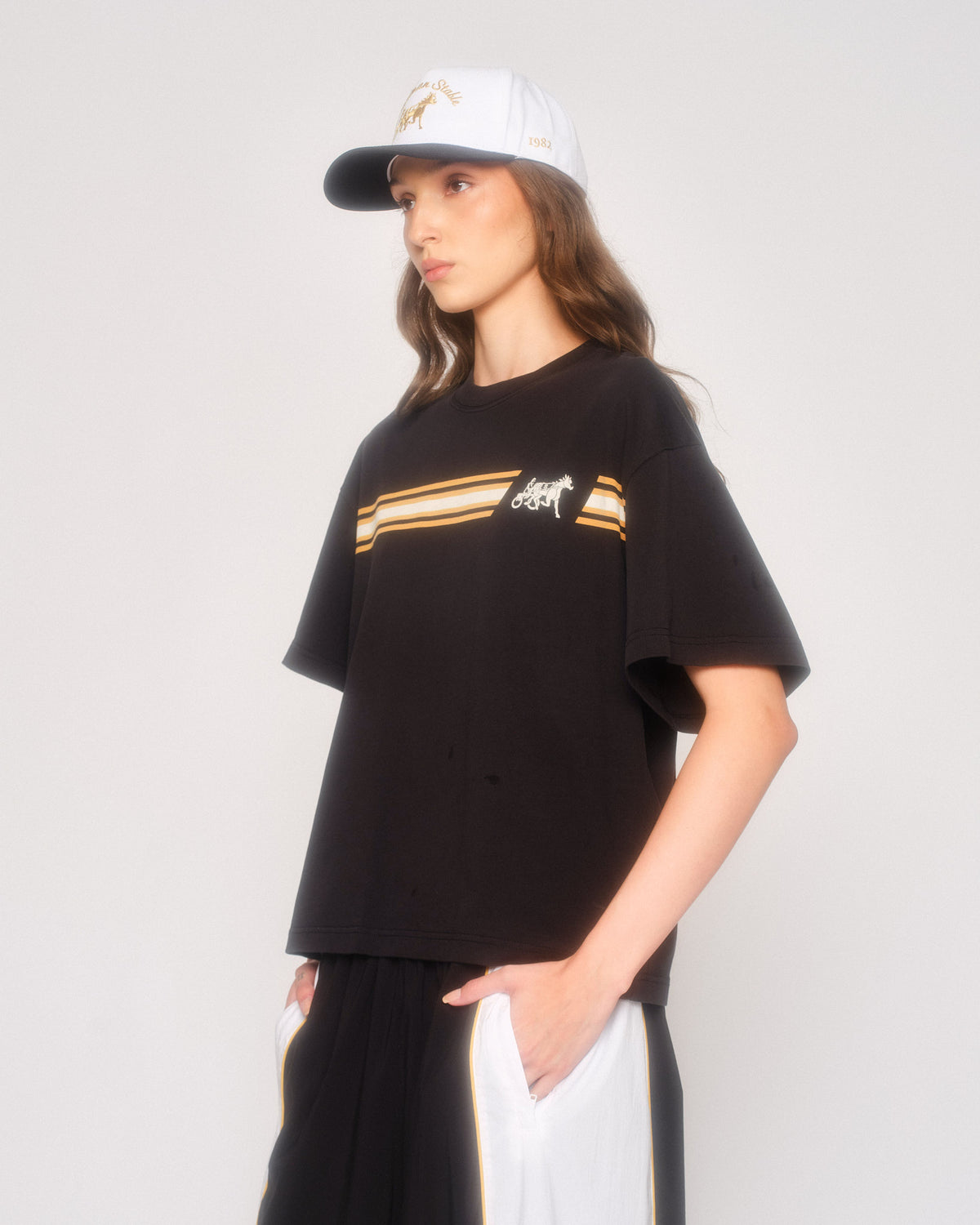 Model in three-quarter view wearing the black Speed Racer cropped tee and white cap