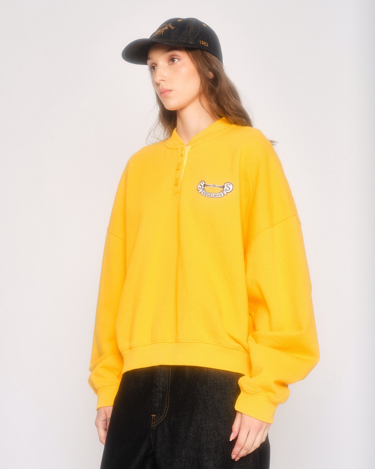 Model in three-quarter view wearing the yellow henley sweatshirt and black cap