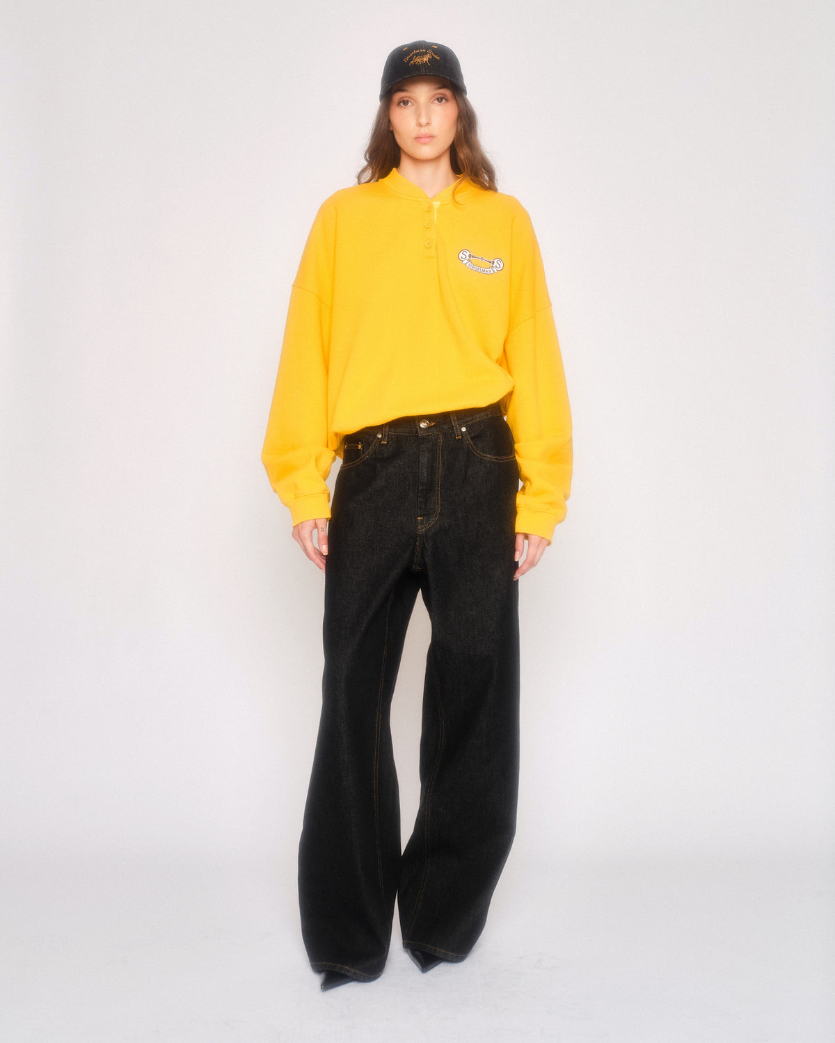 Model wearing the black straight leg jeans with a yellow sweatshirt and black cap