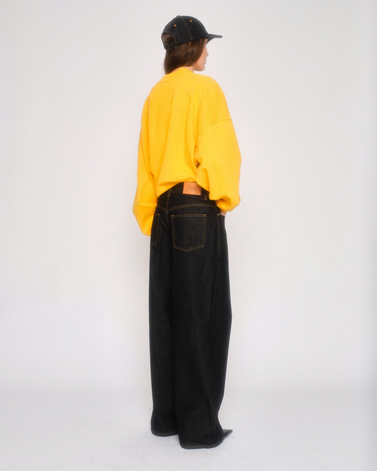 Back view of a model in the black 5 pocket straight leg jeans with a yellow sweatshirt and black cap