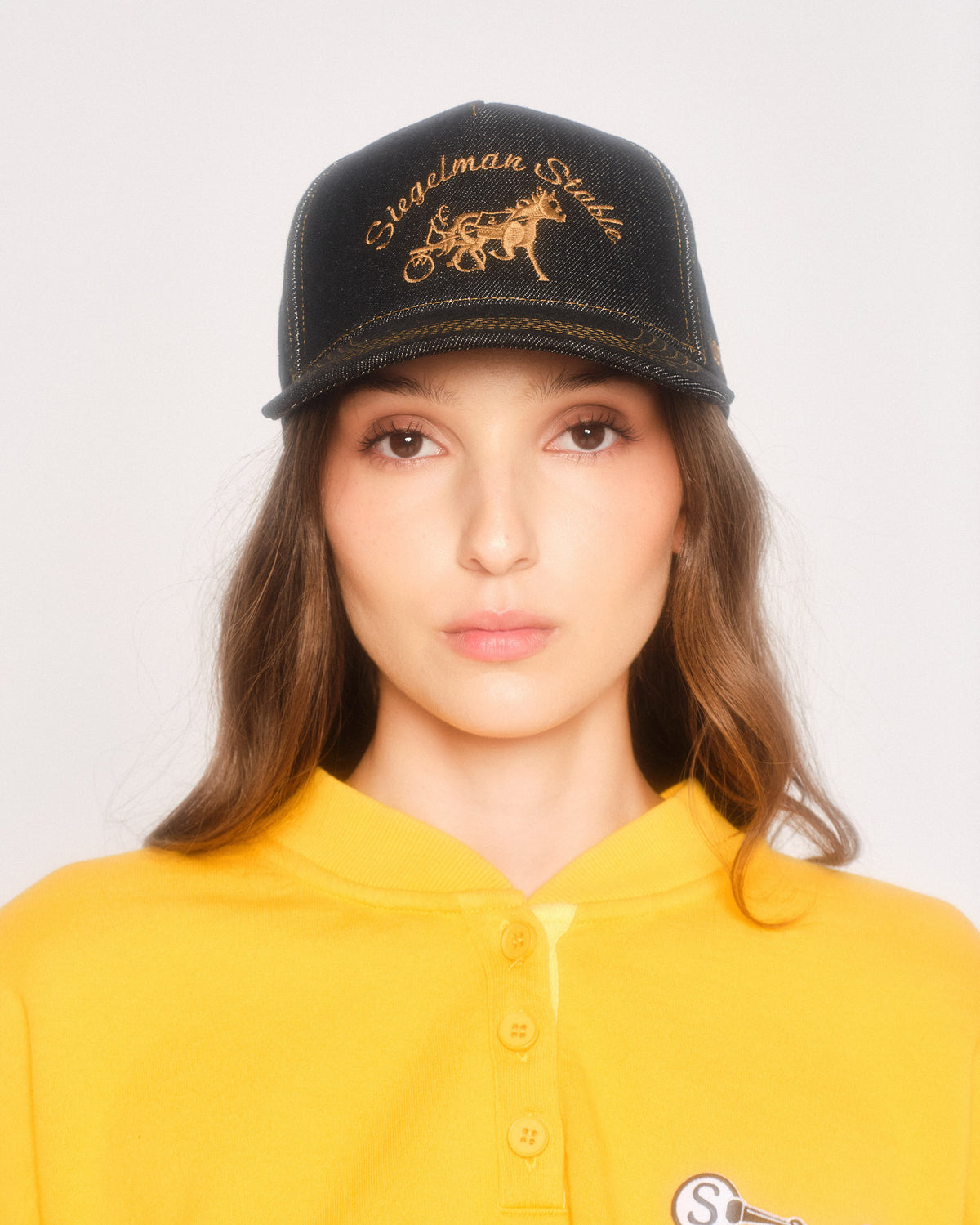 Model wearing the black contrast denim hat with gold embroidery and a yellow henley sweatshirt