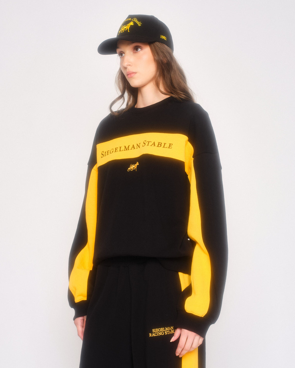Model in three-quarter view wearing the black retro crewneck with yellow stripes and a black cap