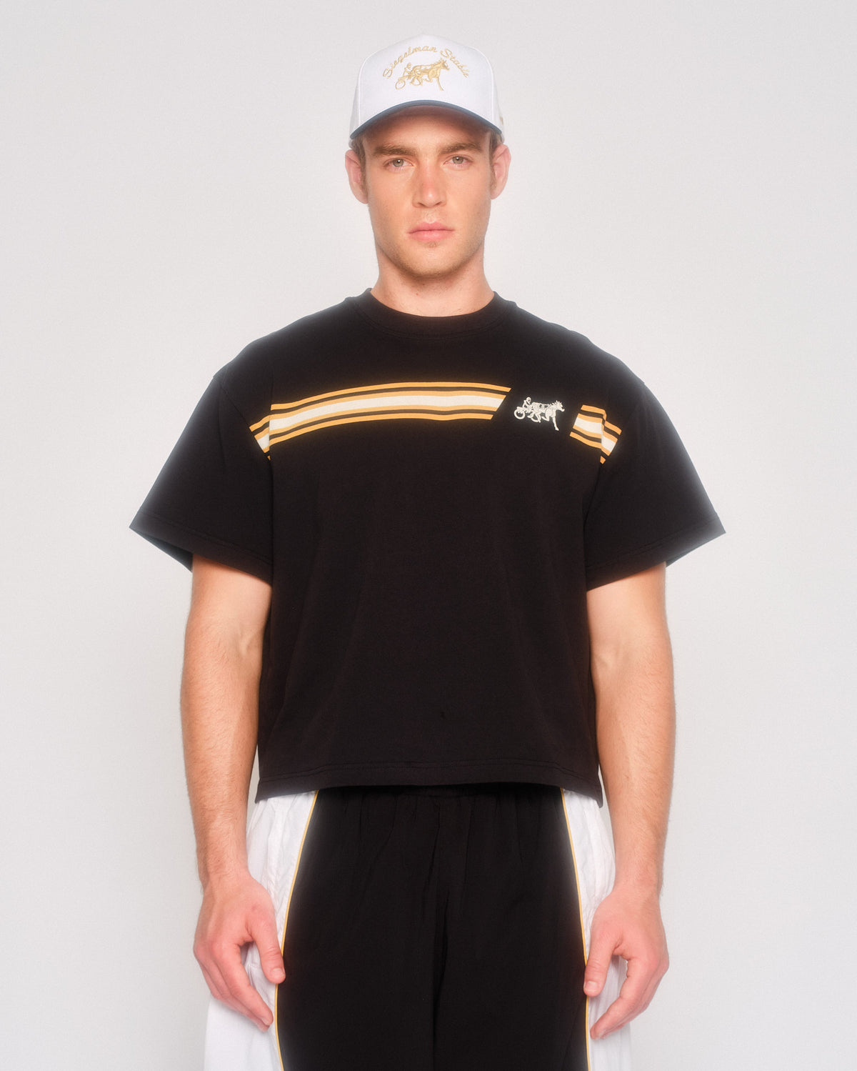 Male model wearing the black Speed Racer cropped tee with striped chest graphic and a white cap