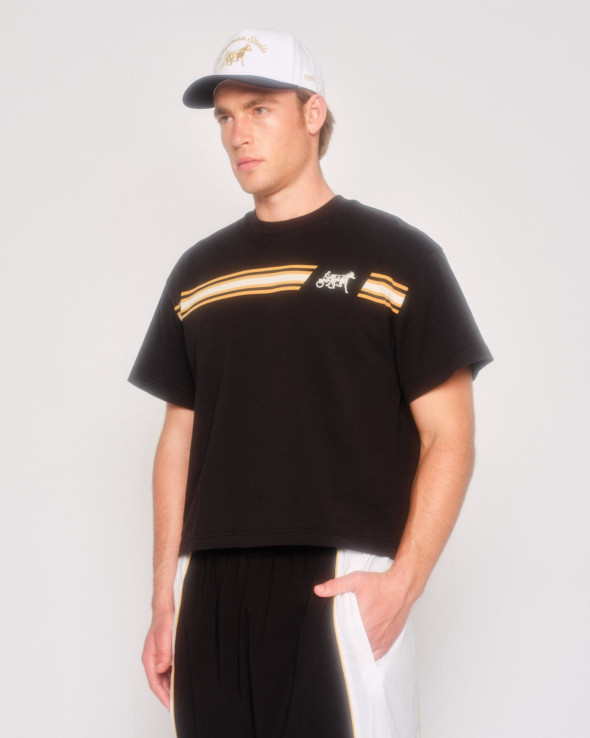 Male model in three-quarter view wearing the black Speed Racer tee, white cap and track pants
