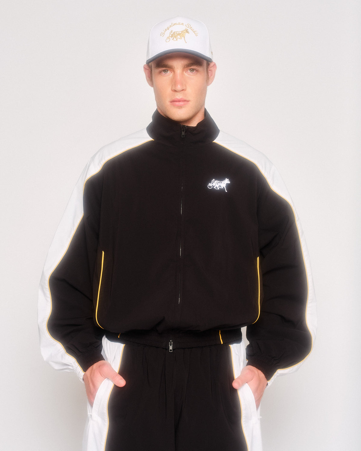 Model wearing the black and white Siegelman Stable track jacket with matching track pants and a white cap