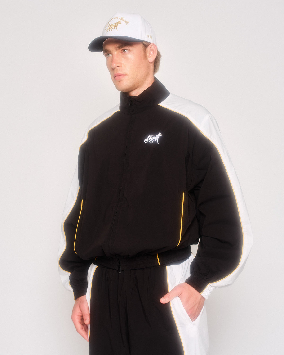 Model in three-quarter view wearing the black track jacket with white sleeves and matching track pants