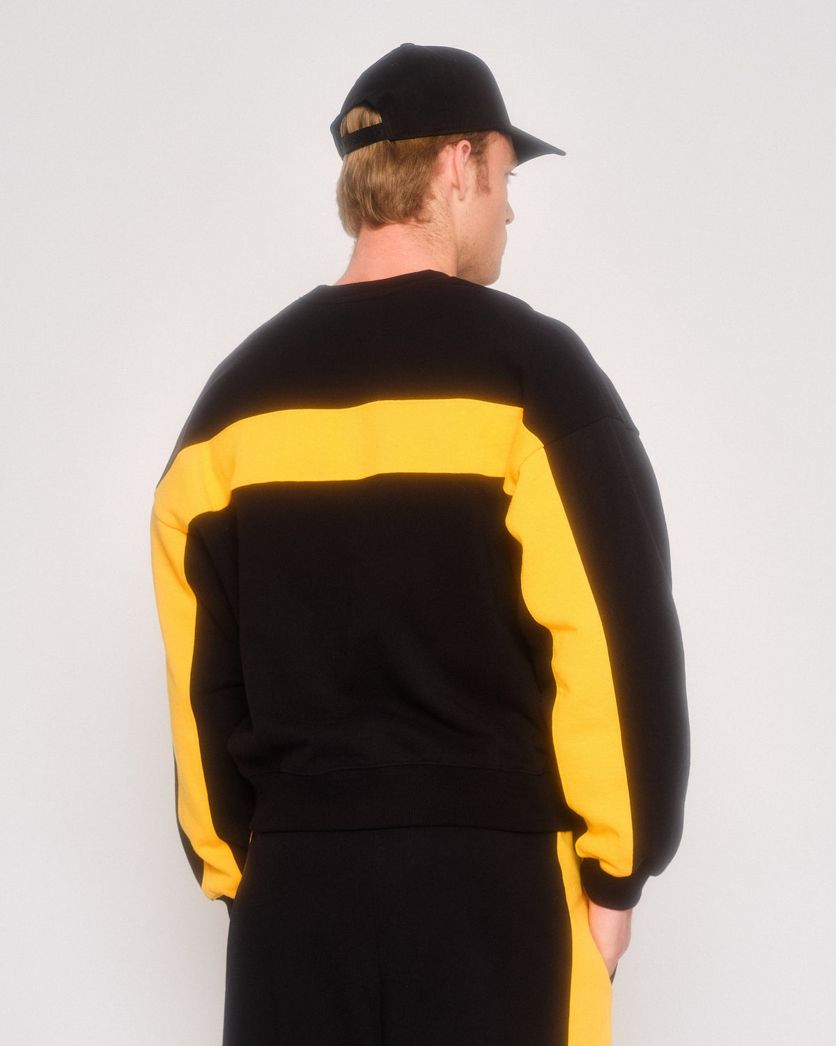 Back view of a male model in the black retro crewneck with yellow back stripe and sleeve stripes