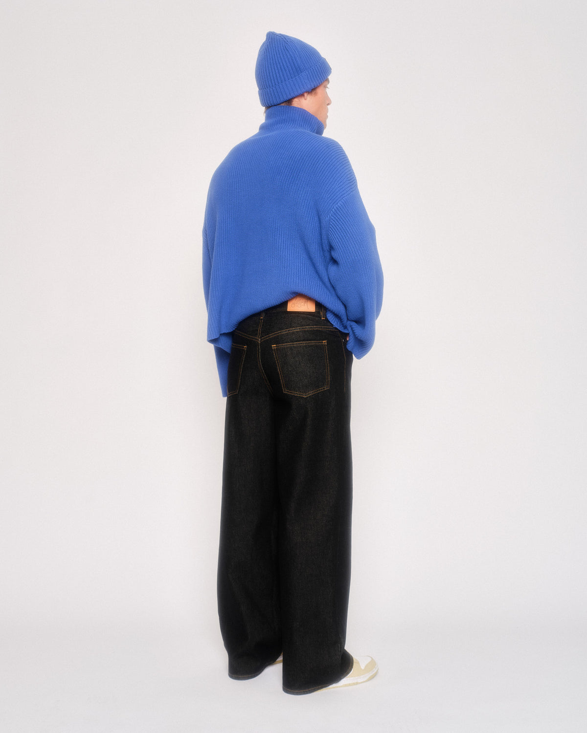 Back view of a model in the black 5 pocket jeans with a cobalt blue zip jacket and blue beanie