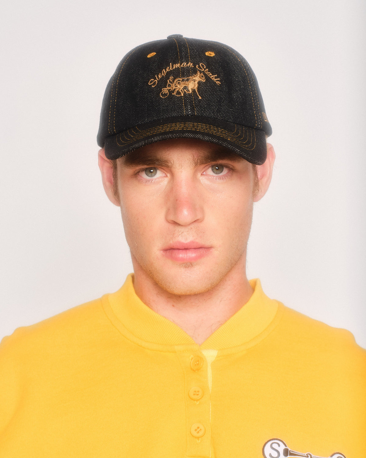 Male model wearing the black contrast denim Siegelman Stable dad hat with a yellow henley sweatshirt