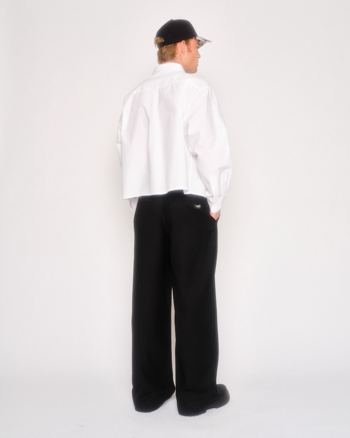 Back view of a male model in the black pleated pants and white button-up shirt