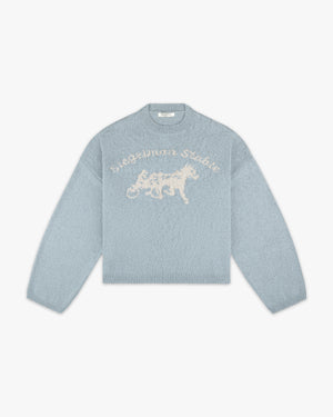 Front view of a dusty blue knit sweater with cream Siegelman Stable script and horse and sulky logo